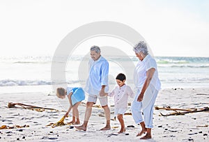 Grandparents and grandchildren holding hands while walking along the beach. Senior couple enjoying summer vacation with