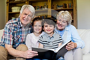 Grandparents and grandchildren holding photo album in living room