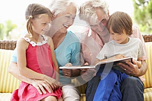 Grandparents And Grandchildren Reading Book On Garden Seat photo