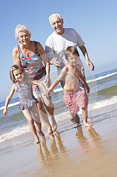 Grandparents And Grandchildren Running Along Beach