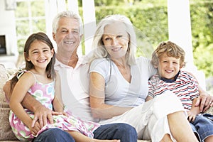 Grandparents And Grandchildren Sitting On Cane Sofa At Home