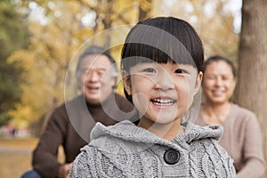 Grandparents and granddaughter in park, smiling and looking at camera