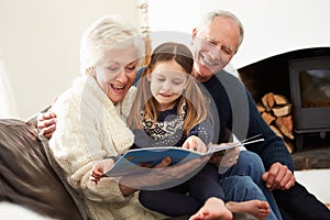 Grandparents And Granddaughter Reading Book At Home Together