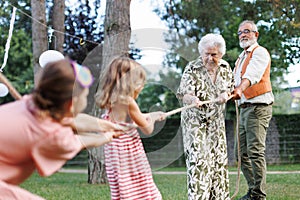 Grandparents have tug of war with their granddaughters. Fun games at family garden party.