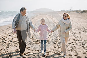 grandparents holding hands with granddaughter while walking on seashore