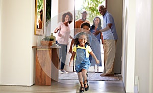 Grandparents At Home Opening Door To Visiting Family With Children Running Ahead