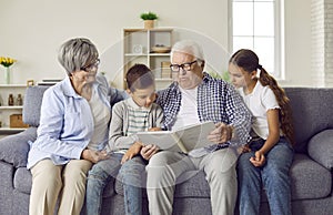 Grandparents and kids sitting on the sofa and reading a story from a children's book