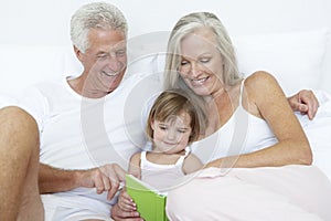 Grandparents reading to granddaughter in bed