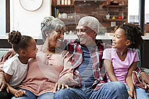 Grandparents Relaxing On Sofa At Home With Granddaughters