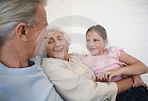 Grandparents Sitting With Granddaughter On Couch