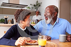 Grandparents Sitting In Kitchen With Grandson Eating Breakfast Before Going To School