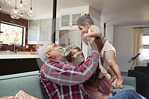 Grandparents Sitting On Sofa Playing With Baby Granddaughter At Home