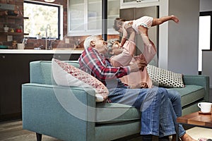 Grandparents Sitting On Sofa Playing With Baby Granddaughter At Home