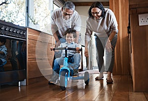 Grandparents, teaching child to ride and bike in kitchen, home or childhood memory of learning with elderly people. Kid