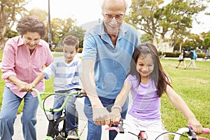 Grandparents Teaching Grandchildren To Ride Bikes In Park