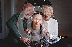 Grandparents and their granddaughter gathered around a Christmas tree, smiling