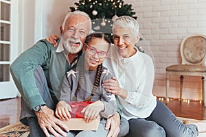 Grandparents and their granddaughter gathered around a Christmas tree, smiling