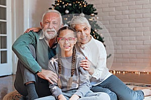 Grandparents and their granddaughter gathered around a Christmas tree, smiling