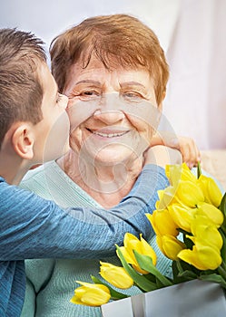 Grandson congratulates grandma on holiday. Grandmother has bunch of yellow flowers. Kindness to senior woman. photo
