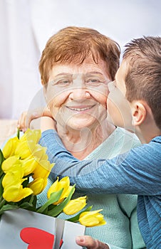 Grandson congratulates grandma on holiday. Grandmother has bunch of yellow flowers tulipan. photo