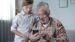Grandson explaining grandfather how to use smartphone, easy app for elderly