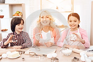 Grandson and granddaughter together with happy grandmother are engaged in cooking in kitchen.