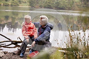 Grandson sitting on his grandfather`s knee at the shore of a lake, Lake District, UK