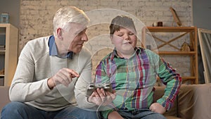 The grandson teaches grandfather to play the console game. An elderly man is learning how to play a video game. Video