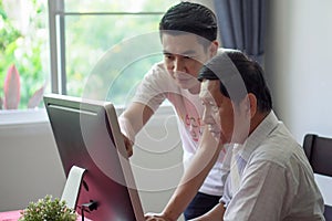 Grandson teaching grandfather how to Using computer and technology in home . young Teacher help senior Man learning to connect photo