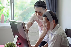 Grandson teaching grandfather how to Using computer and technology in home . young Teacher help senior Man learning to connect