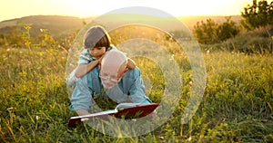 Granfather and grandson laying in grass and reading a book