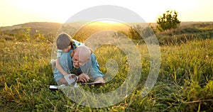 Granfather and grandson laying in grass and reading a book