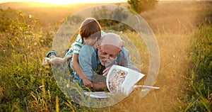 Granfather and grandson laying in grass and reading a book