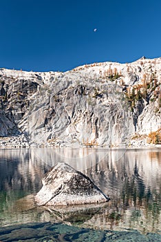 Granite cliffs of Prusik Peak and moon above alpine lake Viviane