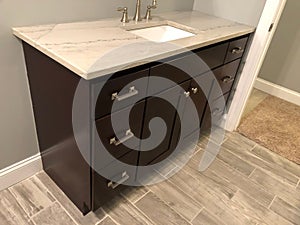 Granite countertop with white sink and chrome faucet on dark wood cabinets, tile floor inside bathroom