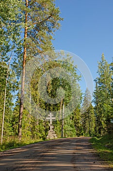 Granite cross on the edge of a dirt road in the forest against the blue sky