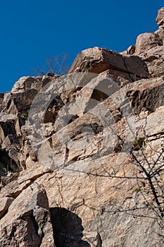 Granite rocks close-up on background blue sky with white clouds, green leaves on treetops.