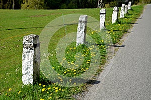 Granite stone bollards old line the mountain road at the moat on the edge of the white curb with a black stripe in a row escort