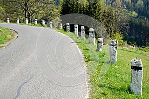 Granite stone bollards old line the mountain road at the moat on the edge of the white curb with a black stripe in a row turn