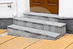 Granite threshold at the entrance door made of brown wood and white facade.