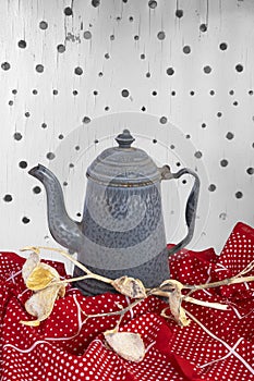 Granite ware tall coffee pot sits on red tablecloth. Star design is on vintage white board background.