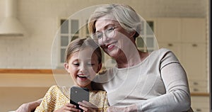 Granny and granddaughter sitting on couch having fun using smartphone