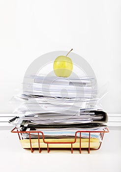 Granny smith apple on stack of documents in desk tray against white wall