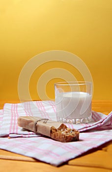 Granola bar and a glass of milk on a towel on wooden table against yellow background