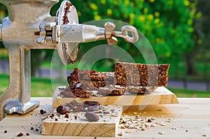 Granola bars with cereals and cocoa beans over a wooden table and a grey hand mill, in a blurred nature background photo