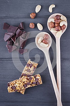 Granola bars with chocolate, nuts, and wooden spoons on the wood