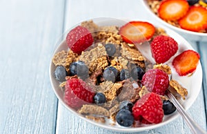 Granola with blueberries and raspberries in white bowl on dark white desk