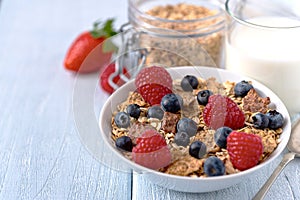 Granola with blueberries and raspberries in white bowl on dark white desk