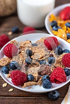 Granola with blueberries and raspberries in white bowl on dark white desk