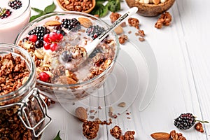 Granola crispy honey muesli with natural yogurt, fresh berries, chocolate and nuts in a glass bowl against a light background,